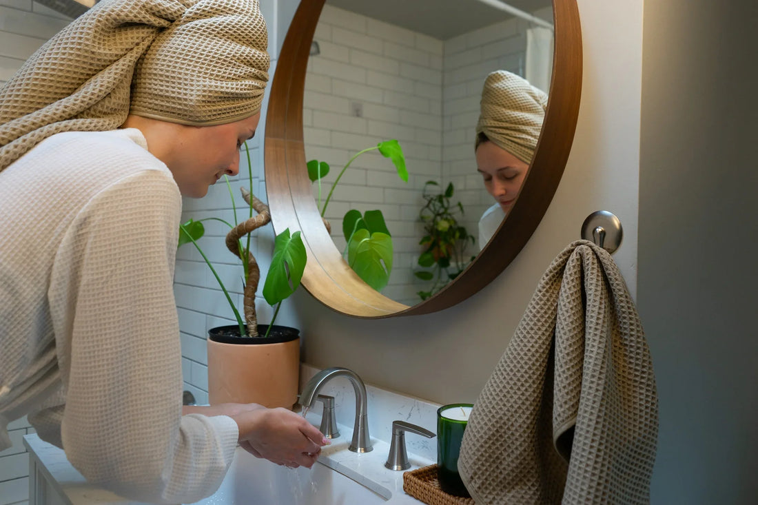 A woman washing her hands at the sink in an elegant bathroom with a plant and a mirror