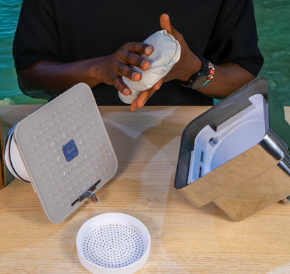 Person holding a shower filter above a showerhead on a wooden surface with water in the background.