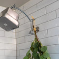 Showerhead attached to extender arm with a plant hanging from it against a tiled bathroom wall