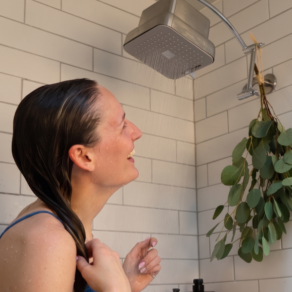 Woman in a bathroom with plants and a mirror.